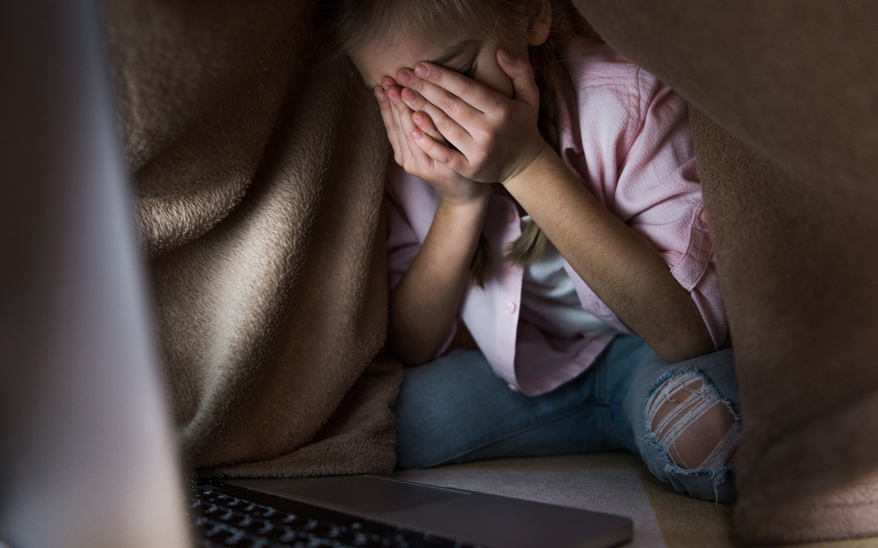 little girl looking at a computer screen crying with her head in her hands