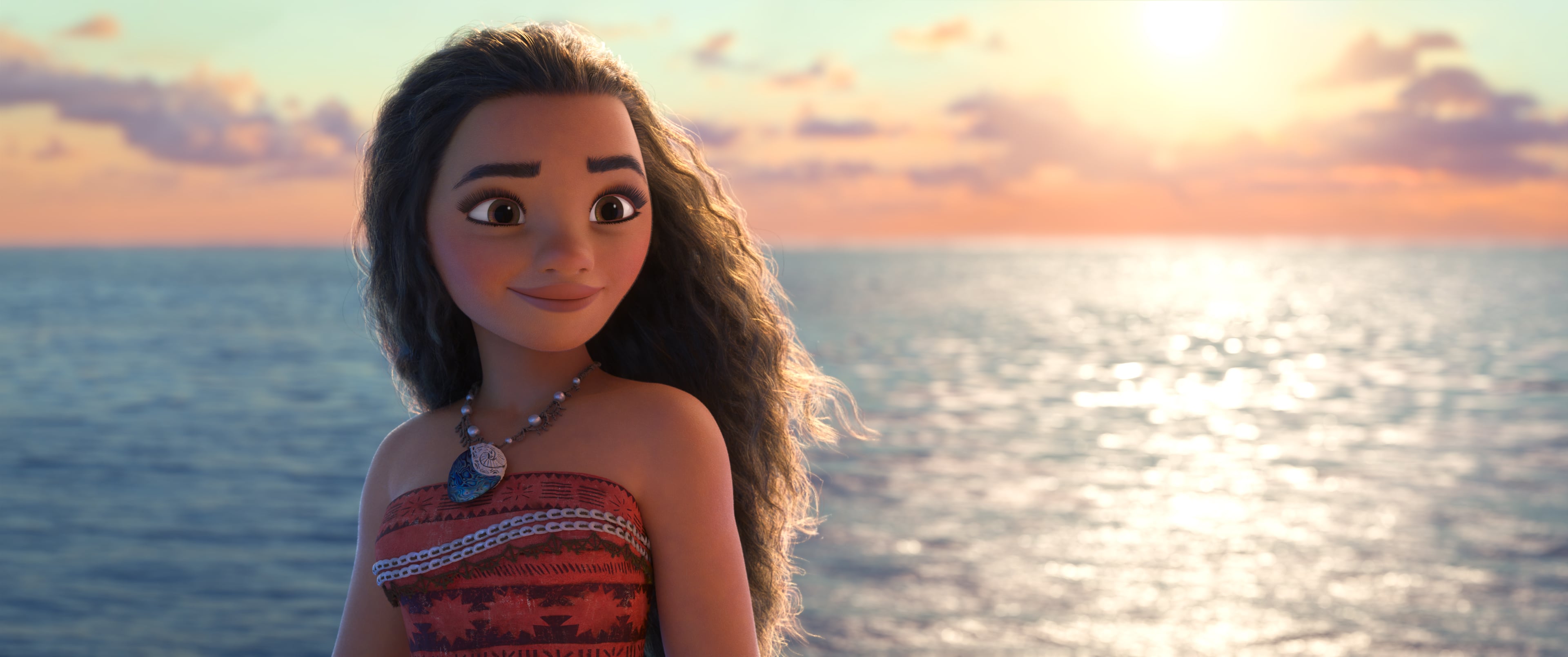 Moana stands on a beach with the sunset behind her. She smiles.