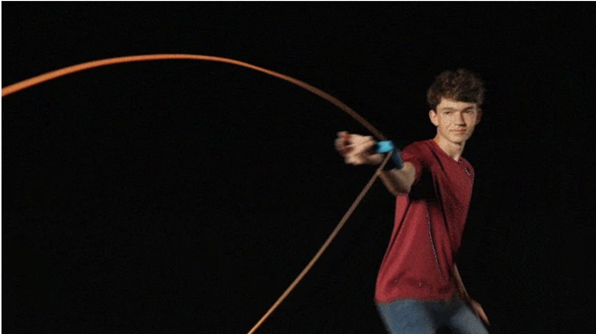 A person demonstrating the ZipString Araçna toy in motion, showing a glowing string looping through the air in front of a dark background.