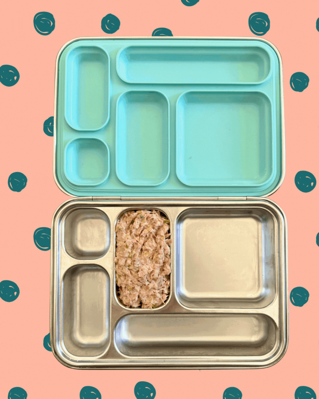 Animated GIF showing a bento-style lunchbox being filled with various nutritious foods, including tuna salad, crackers, sliced cucumbers, a peeled mandarin orange, dried fruit, sliced apples, and rectangular snack bars. The items are placed one by one into the lunchbox compartments against a playful pink and teal polka dot background.