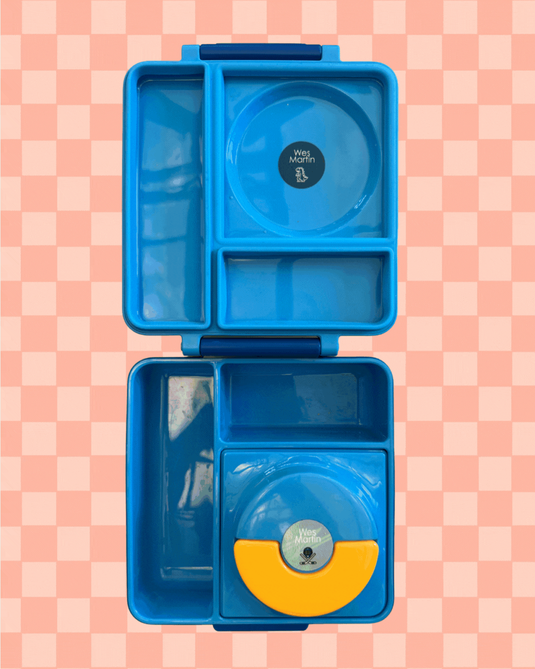 An animated GIF showing a blue bento-style lunchbox being filled with food items—salad with mandarin orange slices, a small baked snack, a packet of roasted edamame, and crispy chicken strips in a round container. The background features a peach-and-cream checkered pattern.